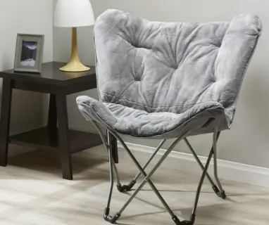 Gray faux‑fur butterfly chair with black metal frame, styled next to a small table and lamp.